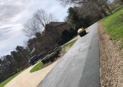 A freshly paved driveway in Charlotte, NC, leading to a suburban house adorned with trees and accompanied by a parked vehicle nearby.