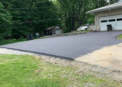 Freshly paved driveway leading to a garage with stacked tires, surrounded by greenery and additional buildings in the background, capturing the charm of Charlotte, NC.