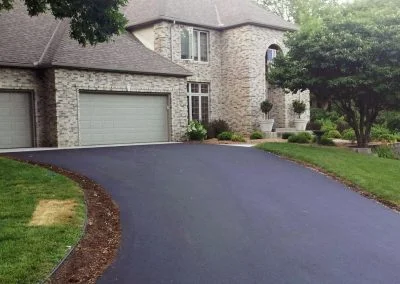 Brick house with a double garage and a newly paved asphalt driveway, surrounded by greenery and trees, located in the charming city of Charlotte.