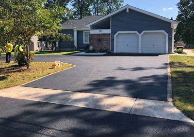 A freshly resurfaced asphalt driveway leads to a charming grey house with a double garage and small front yard, showcasing top-notch asphalt paving that fits perfectly with the scenic beauty of North Carolina.