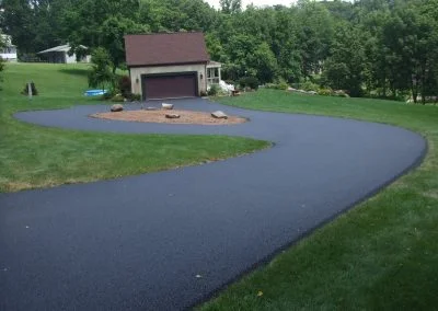 A freshly paved curved driveway leading to a garage, surrounded by a green lawn and trees, brings a touch of North Carolina charm to this serene Charlotte residence.