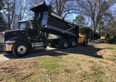 A dump truck is offloading asphalt onto a driveway in Charlotte as workers operate a roller compactor in a residential area.