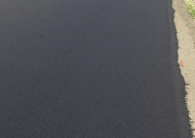 A freshly paved, smooth black asphalt road in North Carolina with a person working in the distance, surrounded by greenery and buildings.