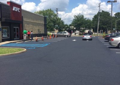 The parking lot of a KFC restaurant in Charlotte, NC, features a few cars parked on the asphalt, with people near the entrance under a partly cloudy sky.