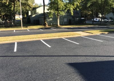 An empty parking lot with freshly painted lines on the smooth asphalt, surrounded by trees and residential buildings in the background, evokes a serene scene typical of North Carolina.