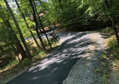 A paved road winding through a wooded area with sunlight filtering through the trees, crafted by expert asphalt paving.