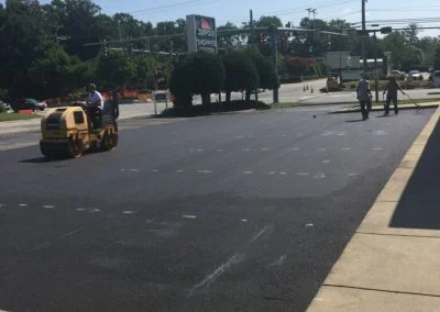Paving crew working on an asphalt parking lot with a roller machine and cones in the background on a sunny day in NC.
