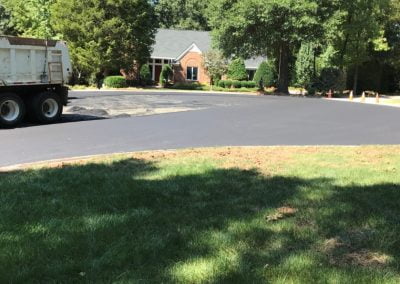 A truck on a newly paved driveway near a brick house with green trees and grass surrounding the area, showcasing the expert asphalt paving skills of NC professionals.