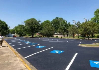 Freshly paved parking lot with new white lines and blue handicap symbols, showcasing quality asphalt paving against a backdrop of trees and a building in beautiful North Carolina.