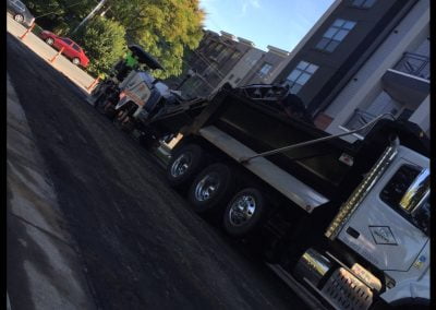 Construction trucks working on asphalt paving near modern buildings and trees on a sunny day in NC.